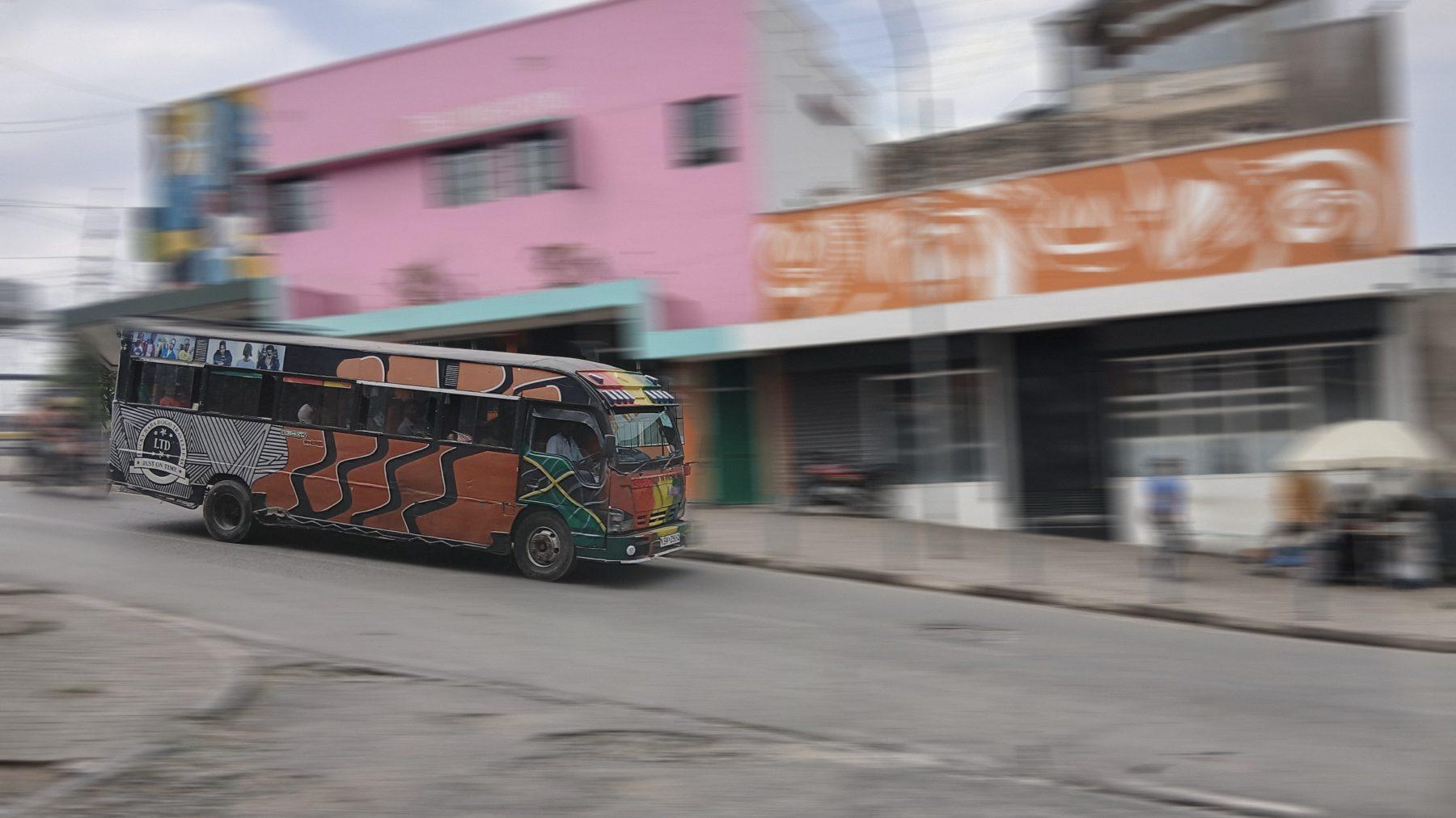A hand-painted matatu speeds past the pink Living Rooms building in Ngara, the street softened by motion blur.